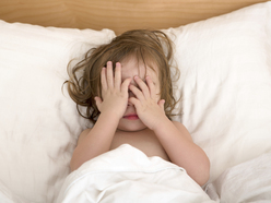 A child lying in bed, covering their face with their hands