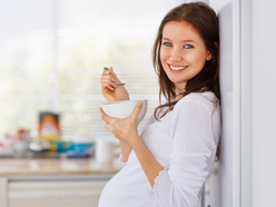 Smiling pregnant woman eating from a bowl with a spoon