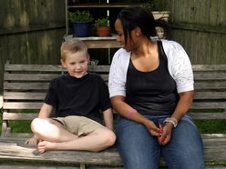 Young boy sitting on a bench next to a woman