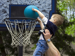 Dad helping toddler son dunk a basketball