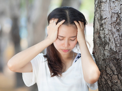 Dizzy woman holding her head and leaning against a tree