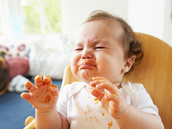 Baby in his highchair, covered in food and crying