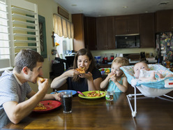 Mom, dad, toddler and baby all eating dinner together at table 