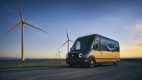 An Amazon Rivian van driving next to a wind farm during sunset. 