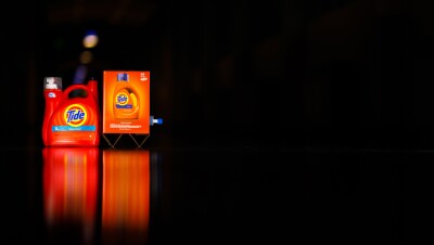 Two different types of packaging for Tide laundry detergent photographed against a black background. The package on the left is plastic. The package on the right is cardboard.