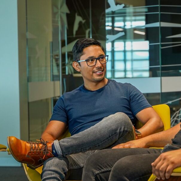 An image of two men seated in chairs talking in an office setting.