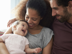 A baby smiling and looking up at their parents