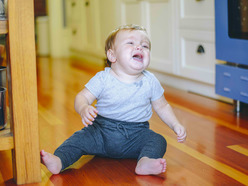 A baby sitting on a kitchen floor and crying