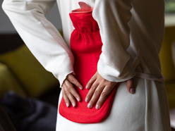 A woman pressing a heating pad against her lower back.