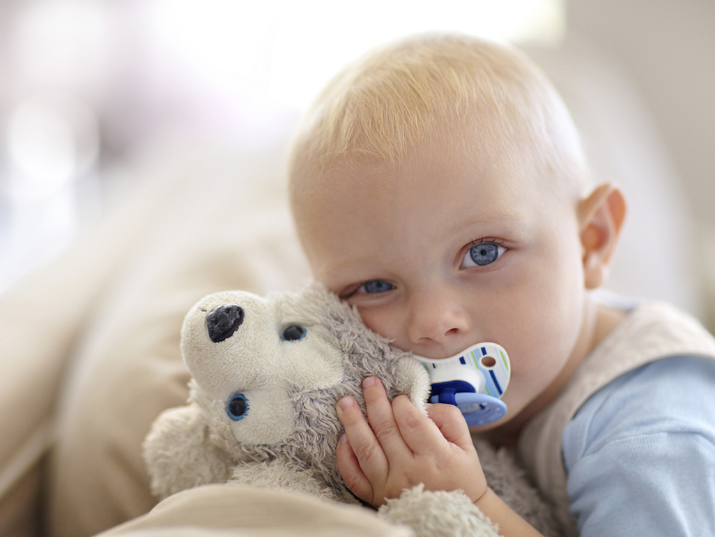 little boy with pacifier hugging his stuffed toy