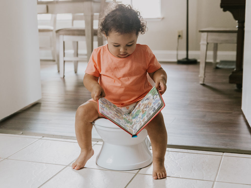 toddler sitting on potty with book