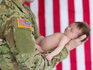 military service person holding a sleeping newborn baby on his forearm