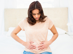 A pregnant woman sitting on the edge of a bed with her hands on her stomach