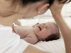 bebé en la cama llorando mientras su mamá lo mira