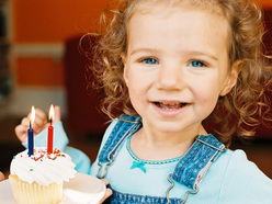 Mädchen mit einem Muffin, in dem zwei brennende Kerzen stecken