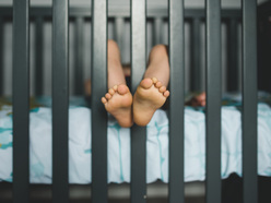 A toddler laying down with their feet sticking out of a crib