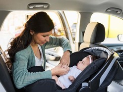 A woman buckling a baby into the car safety seat.