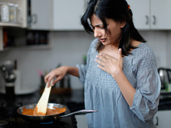 Suffering from morning sickness, a woman looks nauseous as she cooks breakfast.