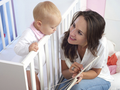 Baby standing in her cot looking at her mum kneeling on the floor