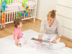 Mom reading to toddler daughter in child's bedroom