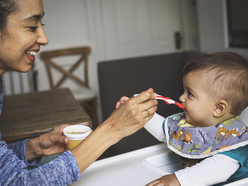 Baby in a highchair, being fed puréed vegetables from a spoon