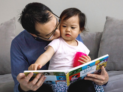 Dad reading book to daughter on sofa