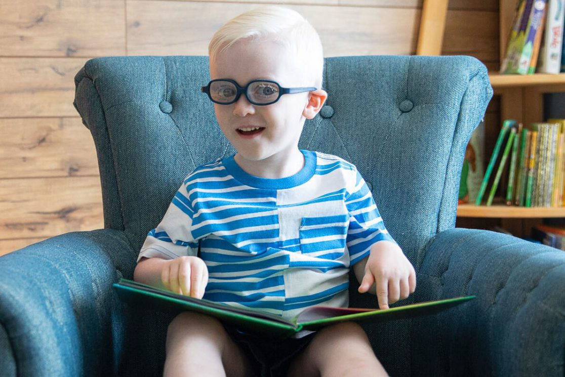 A child sitting in a blue armchair and reading a braille storybook.