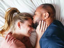 A man and woman lying in bed together, the man is kissing the woman's forehead.