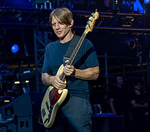 Chaney, aged 52, holds his guitar firmly. He wears a blue T-shirt and blue pants.