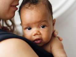 Baby with an uncomfortable expression resting her head on her mother's shoulder