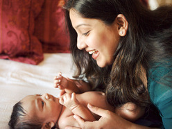 Mum bending over and smiling at baby lying on the bed with no clothes on