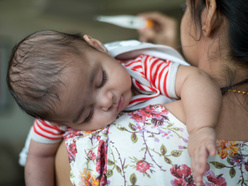 Mum looking at a thermometer as she carries her unwell baby