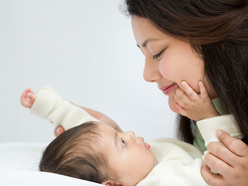 Mom smiling at her baby lying on the bed as he looks up to her