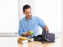 Ein Mann packt Pausenbrot und einen Apfel in eine Tasche