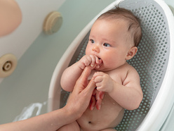 Baby in bath seat grasping mum's finger