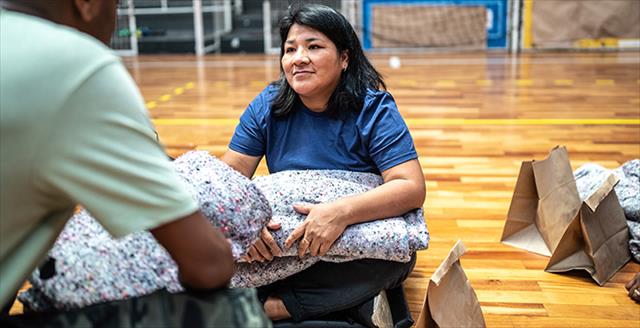 couple sitting on a gym floor holding sleeping blankets