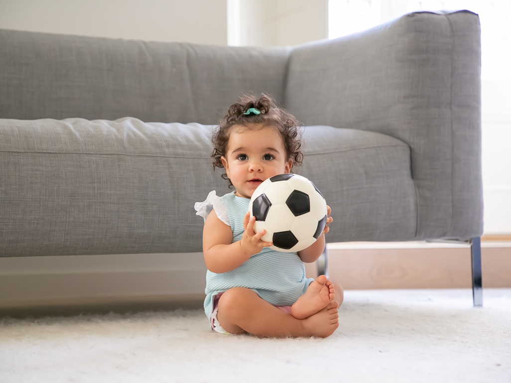 Toddler girl sitting by sofa holding football