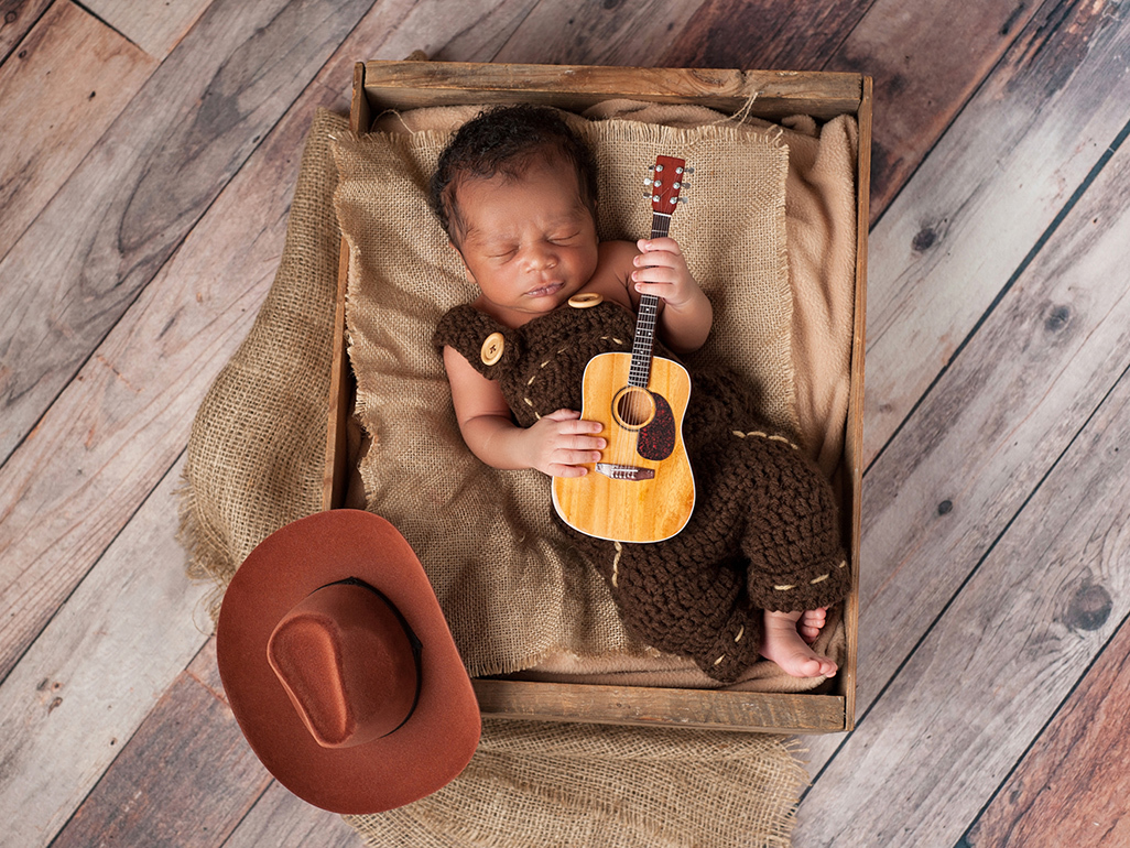 Newborn baby dressed as a cowboy holding a small guitar