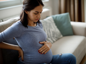 Pregnant woman sitting on sofa and looking pained