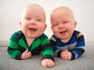 Two baby twins on their tummy looking at the camera