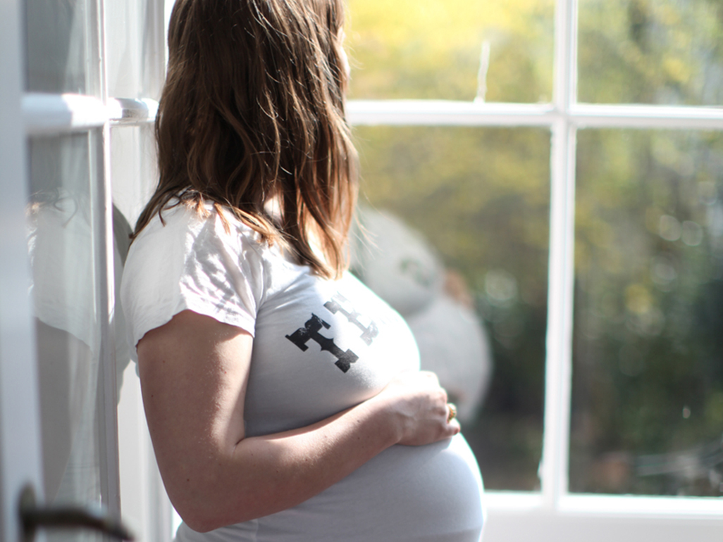 Pregnant woman with hand on large bump looking out of a window