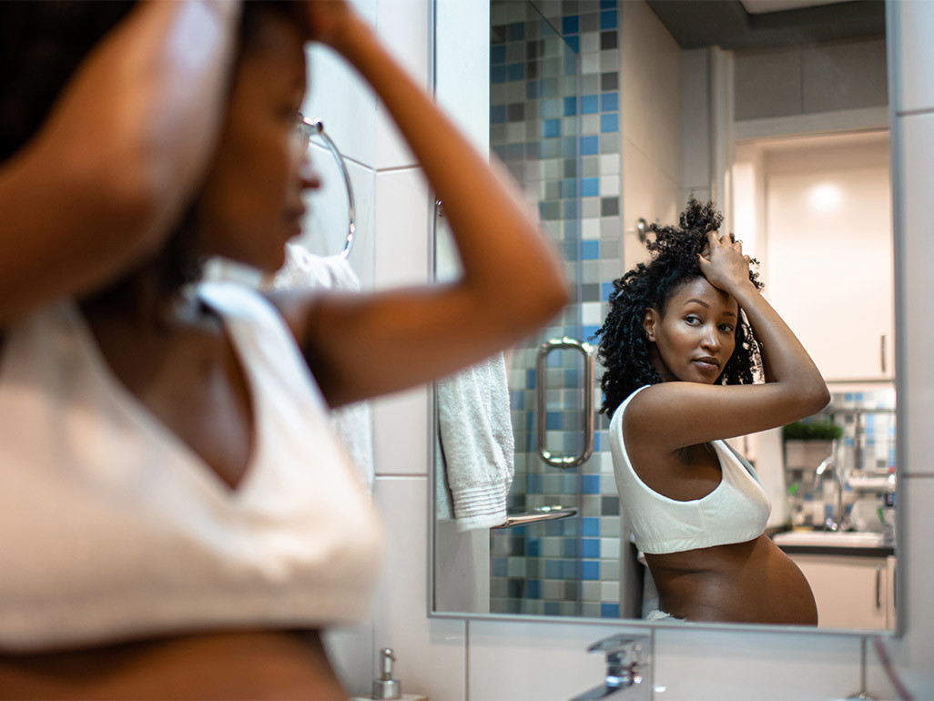 A pregnant woman looks at her reflection in bathroom mirror