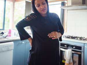 Heavily pregnant woman holding her back and her bump with eyes closed and a pained expression on her face