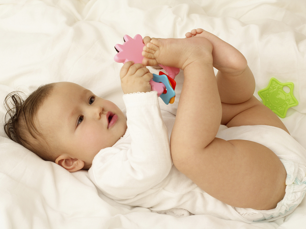 baby holding a colourful plastic teething ring