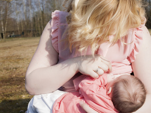 Mum outside in warm sunshine calmly breastfeeding baby while stroking baby's little finger