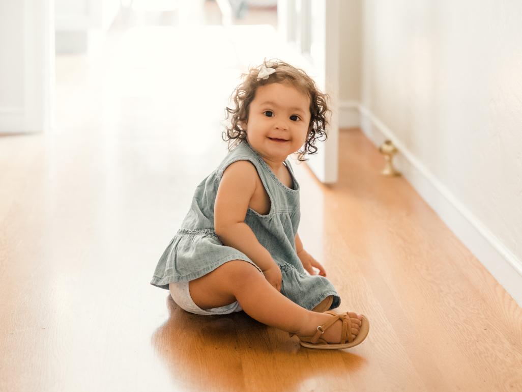 Smiling toddler girl sat on wooden flooring