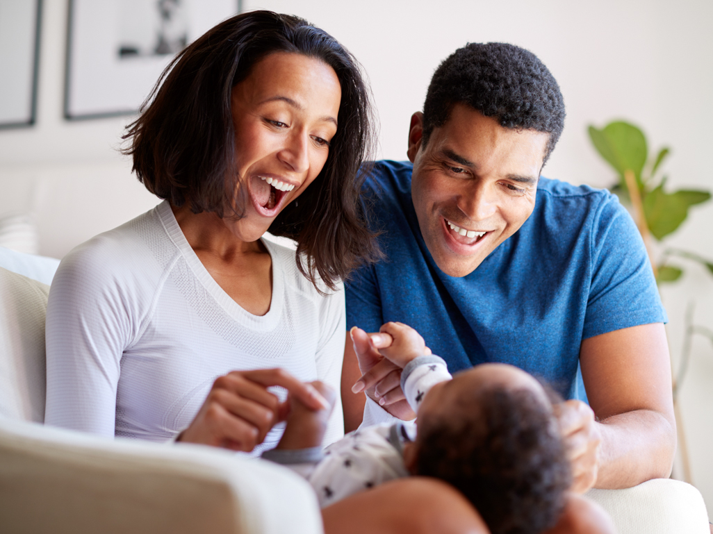 Two parents smile and laugh with their baby