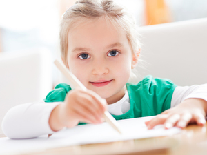 girl in green top writing on paper with pencil