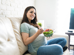 Mulher branca grávida branca sentada no sofá comendo salada