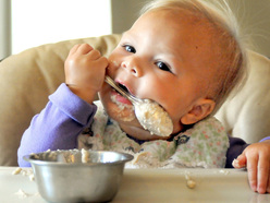 Messy one year old spoon-feeding herself